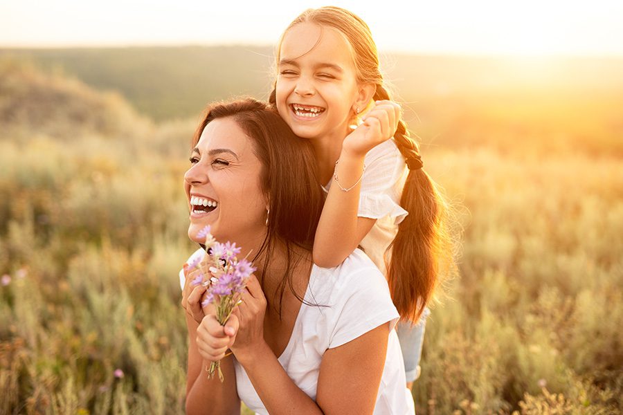 Blog - Closeup Portrait of a Cheerful Mother and Daughter Having Fun Picking Flowers in a Field at Sunset