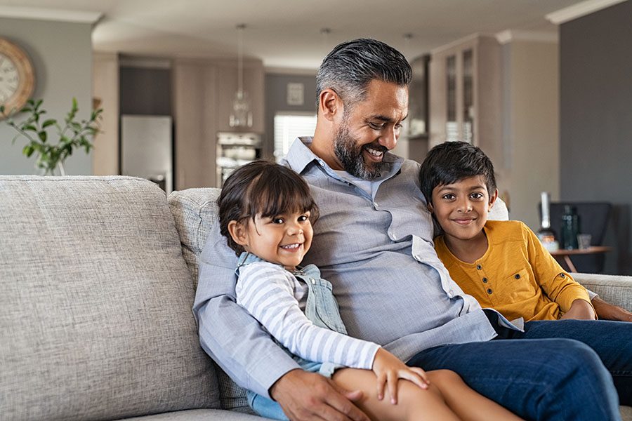 Personal Insurance - Closeup Portrait of a Cheerful Father Sitting on the Sofa in the Living Room with His Two Kids